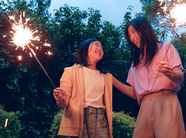 A mom and daughter holding sparklers outdoors