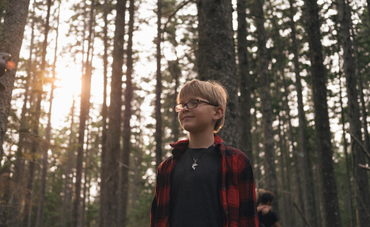 A young boy standing outdoors in the woods