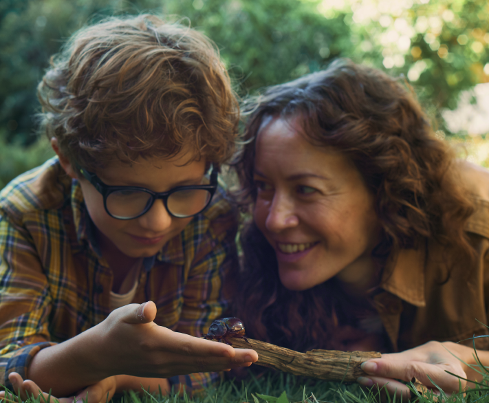 A mother and her son outdoors observing a beetle